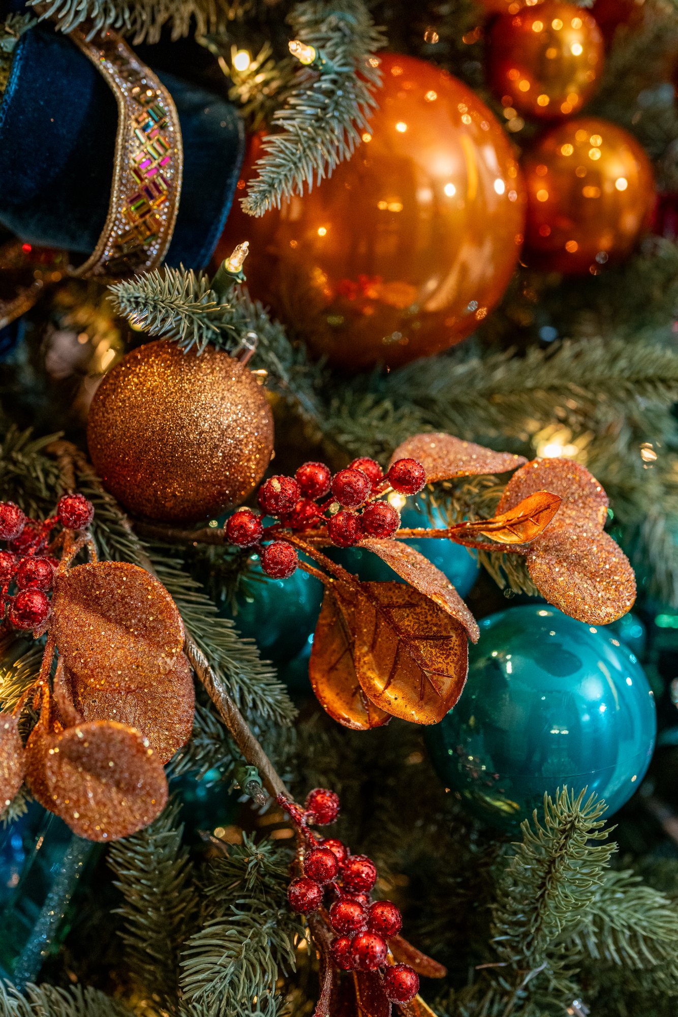 Glittered copper eucalyptus leaves and crimson berries nestled among teal ornaments