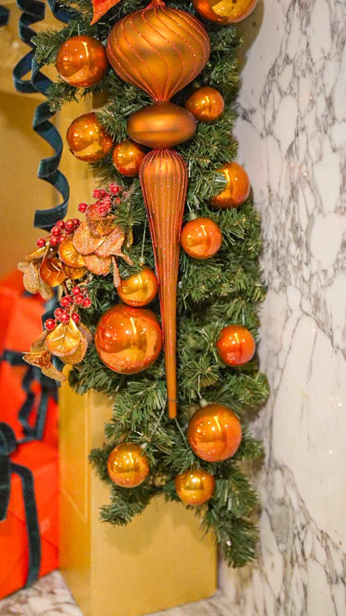 Vertical garland drop featuring copper finial ornaments, glittered leaves, and red berries against white marble