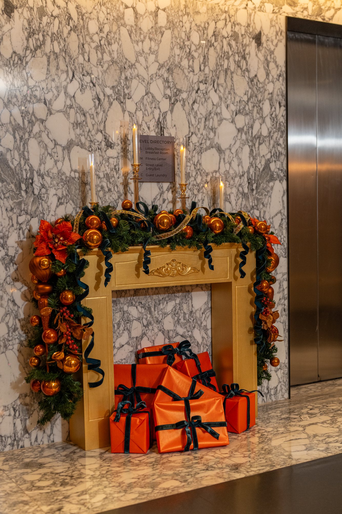 Gold fireplace mantel styled with copper ornament garland, flameless candles, and gifts in persimmon paper with teal velvet ribbon