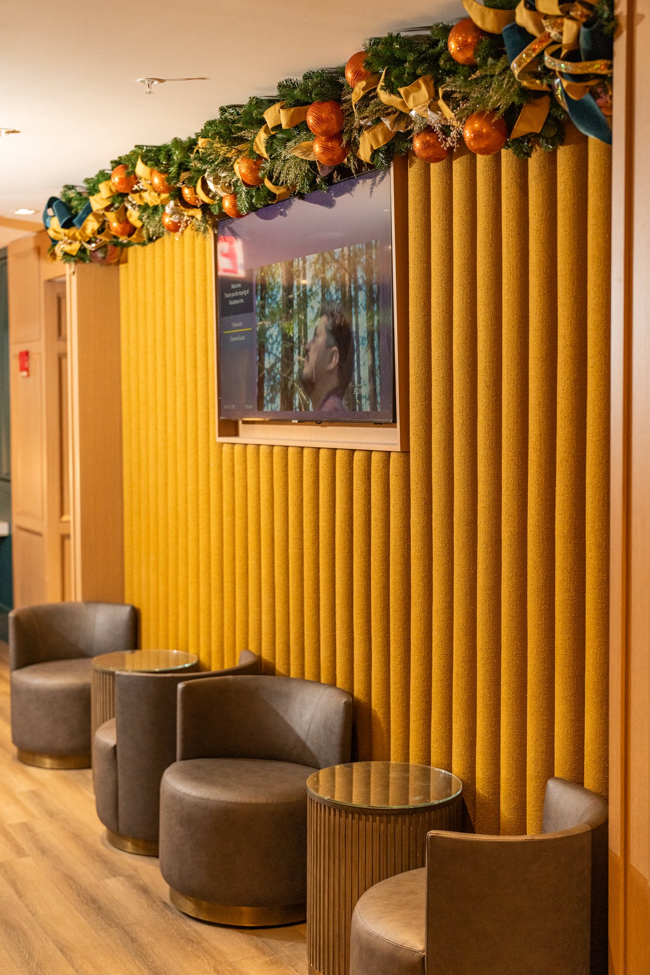 Evergreen garland with copper ornaments and teal-and-gold velvet bows above a hotel lounge seating area
