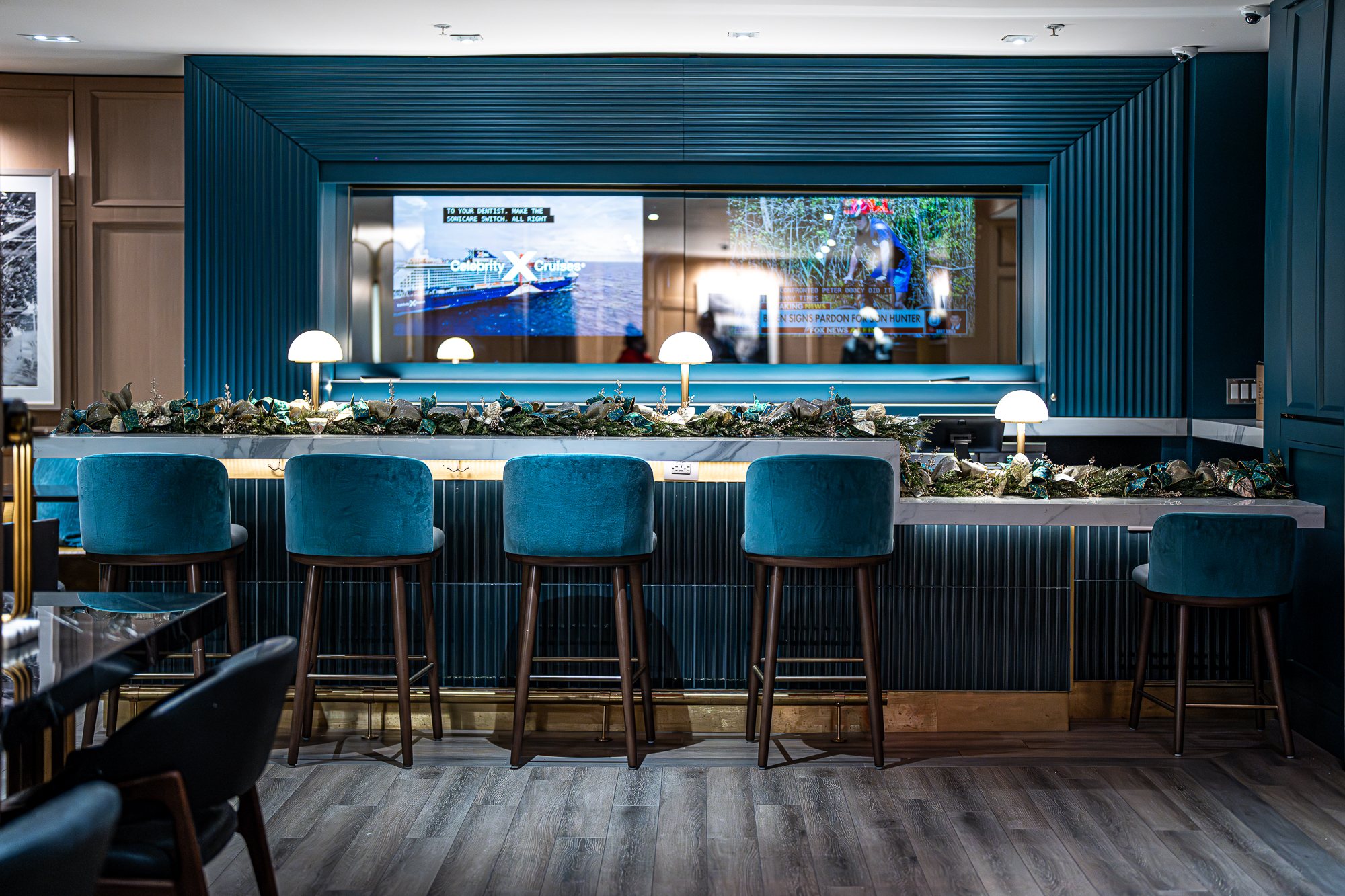 Marble reception bar with teal velvet stools and an evergreen garland accented with gold and teal ribbon at the Hilton