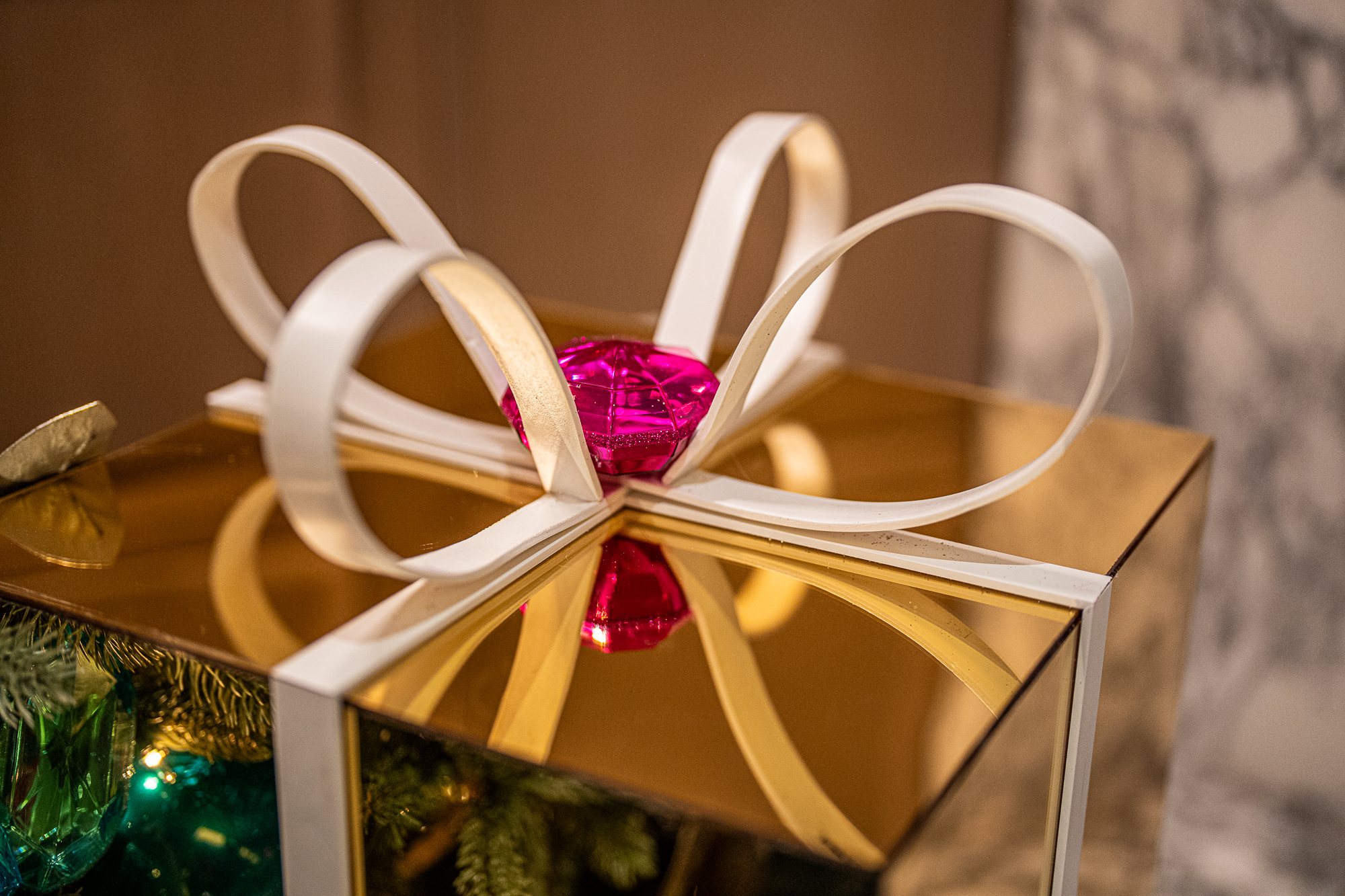 Mirrored gold gift box tied with a white bow and pink gem accent