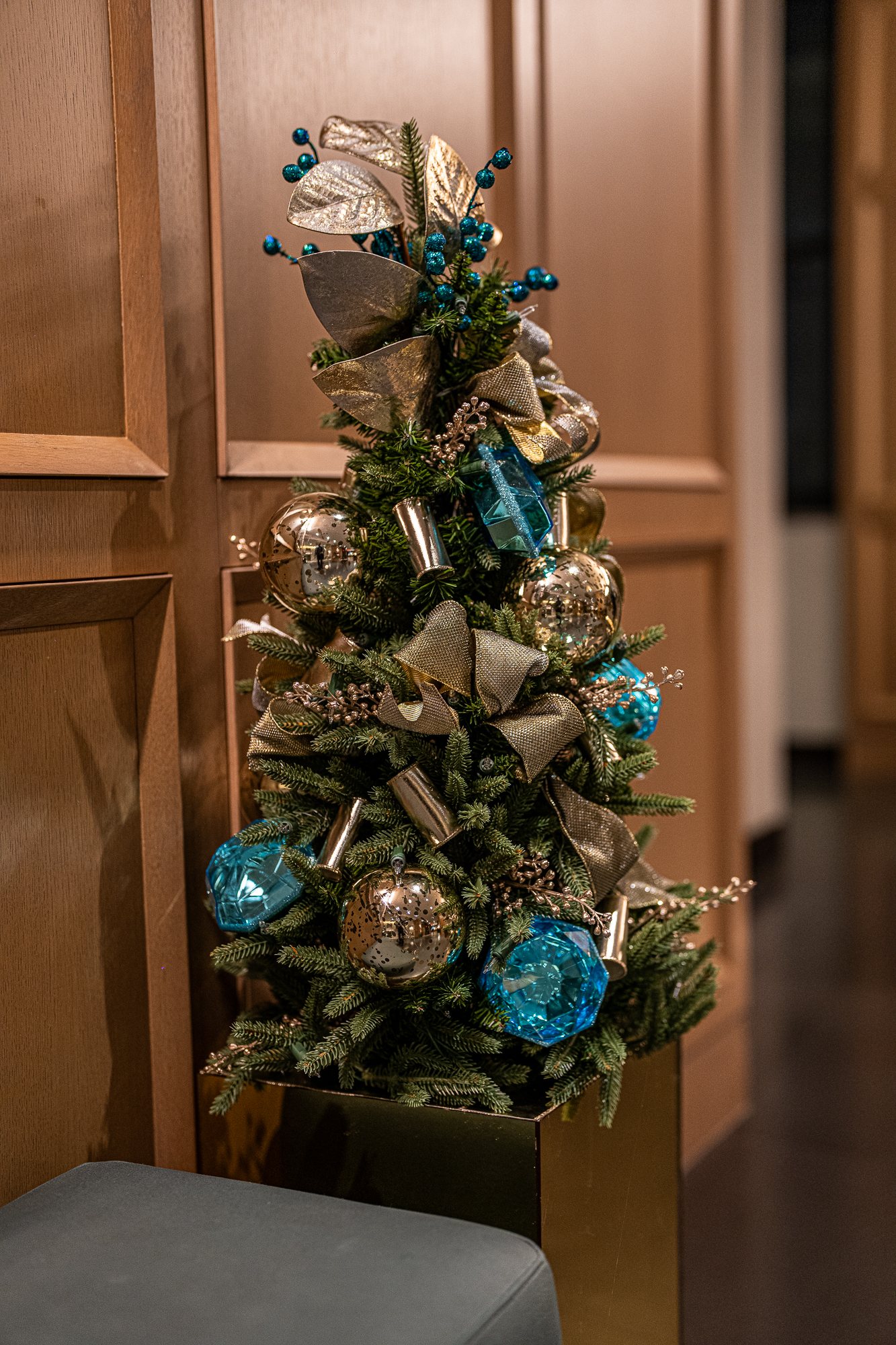 Tabletop Christmas tree with gold mercury-glass ornaments and aqua gems against wood paneling