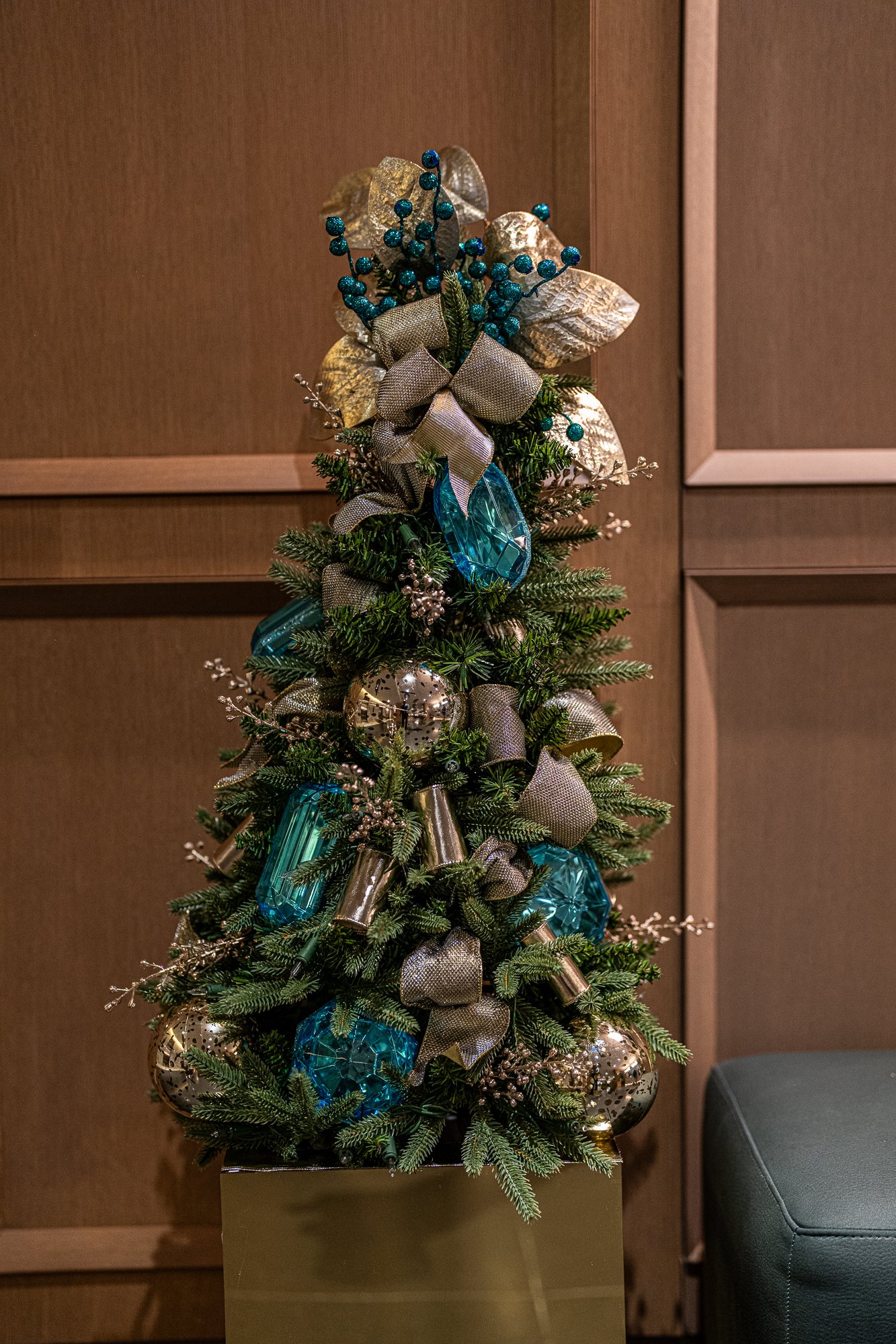 Tabletop Christmas tree in teal, gold, and silver with mercury-glass ornaments on a gold pedestal