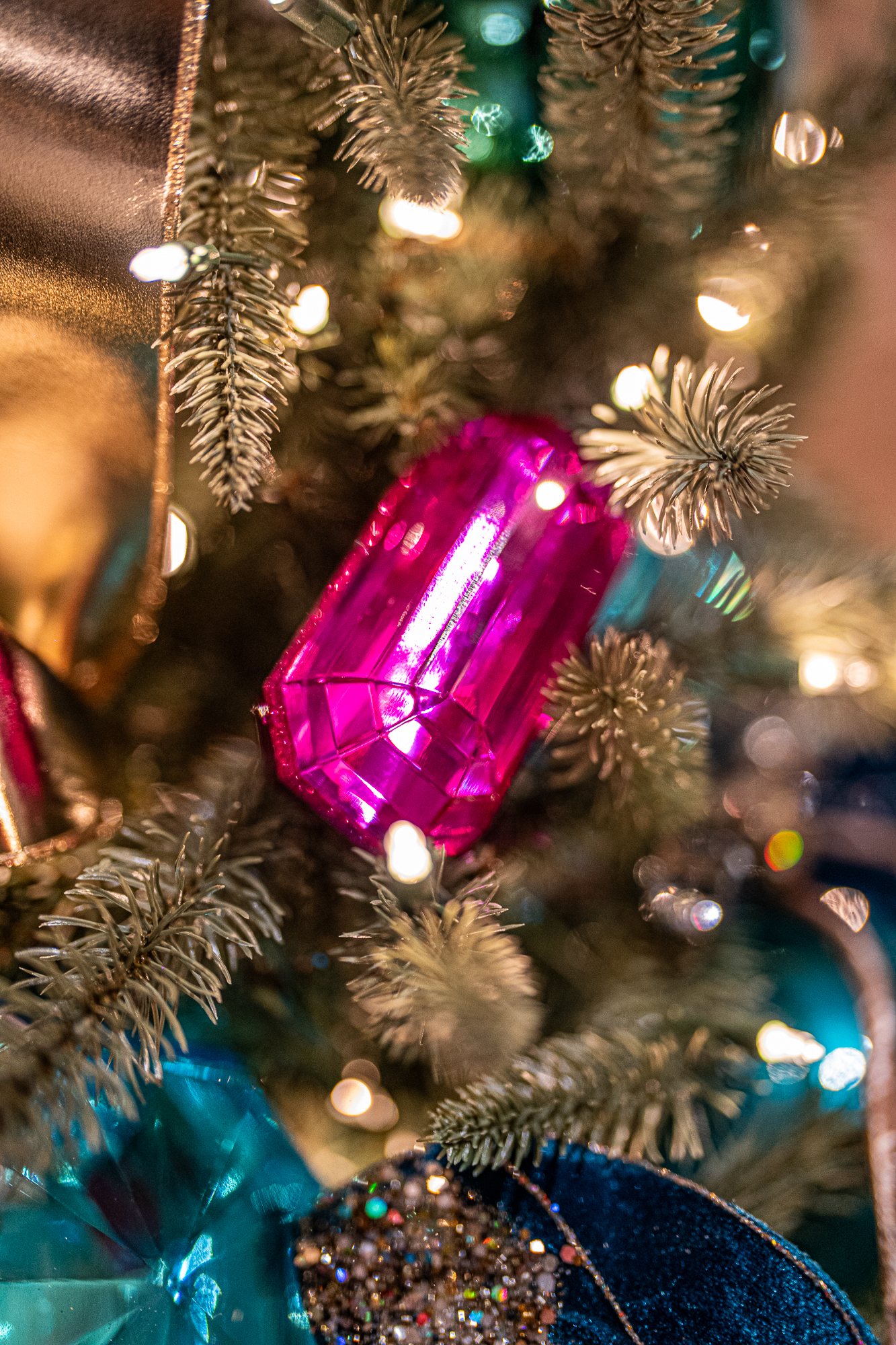 Faceted fuchsia gem ornament nestled among teal ornaments and velvet leaves