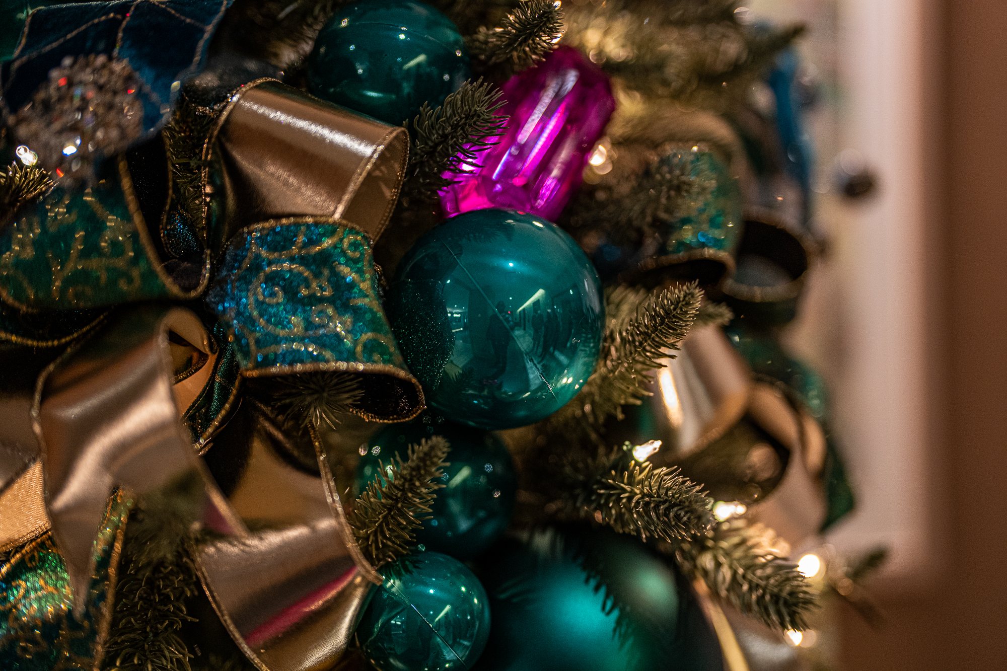 Cluster of teal ornaments, gold mesh ribbon, and a fuchsia gem on the jewel-tone tree
