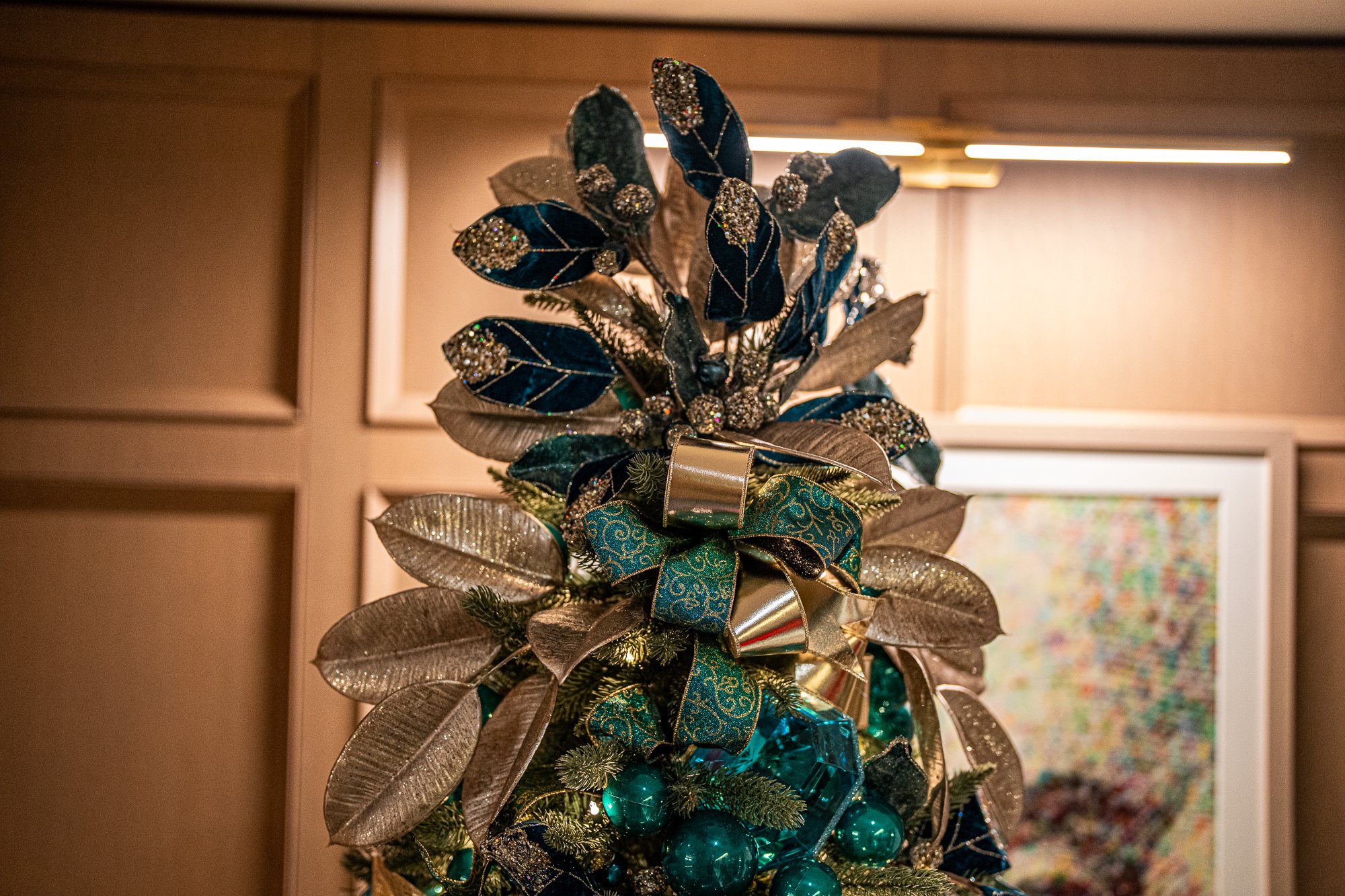 Gilded magnolia-leaf tree topper with teal velvet leaves on the jewel-tone lobby tree